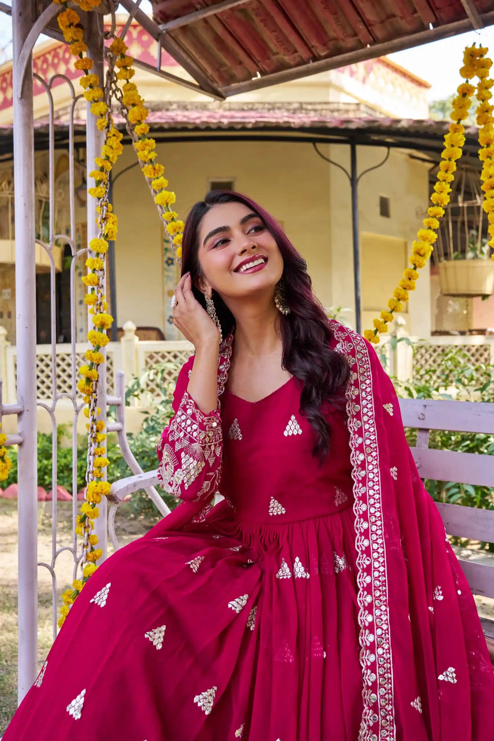 Woman in a red traditional outfit sitting on a swing with yellow flowers in the background